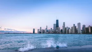 Stadssilhuett i Nordamerika vid en sjö med skyskrapor och vågor som slår mot strandkanten.