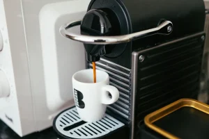 Den vanligaste källan till koffein visas när kaffe bryggs i en kapselmaskin och espresso rinner ner i en vit kopp på droppbrickan.