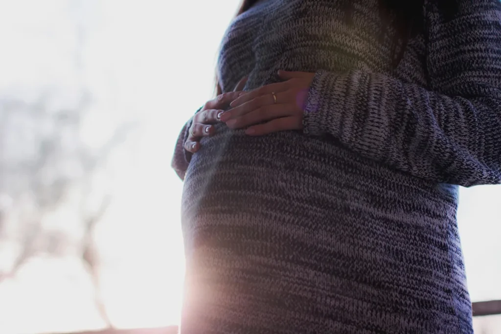 Koffein och graviditet illustreras av en gravid kvinna som håller händerna över magen i lugn hemmiljö med mjukt ljus.