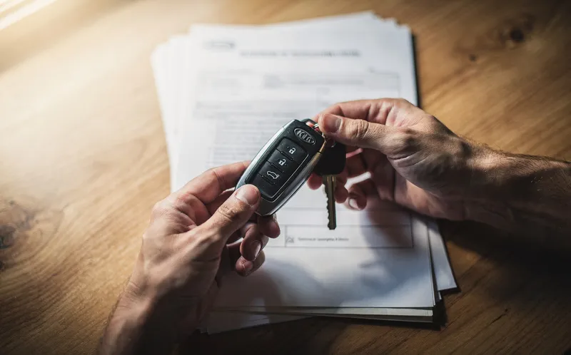 Händer som växlar bilnycklar över papper på skrivbord