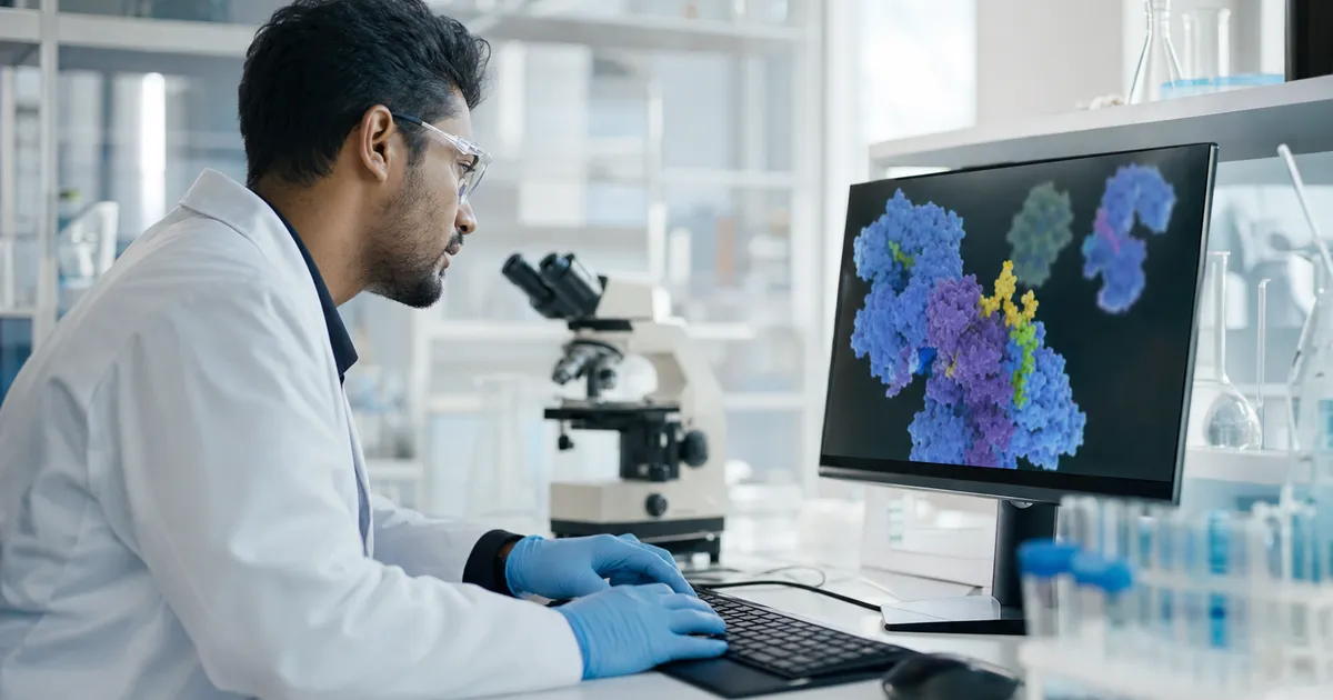 Forskarens händer arbetar med laboratorieprover, datorskärm med grafer i bakgrunden